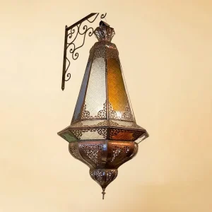 A tall, teardrop-shaped Moroccan lantern featuring intricate bronze filigree metalwork and alternating panels of amber and frosted white stained glass, suspended from a decorative scrollwork wall bracket against a neutral background.
