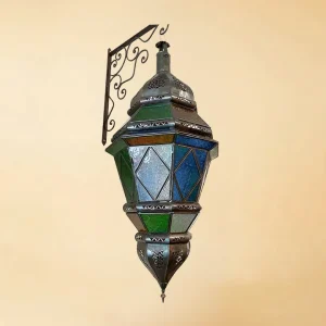 A large, ornate Moroccan hanging lantern with multi-colored stained glass panels in green, blue, and white, featuring intricate bronze metalwork and suspended from a decorative scrollwork wall bracket against a neutral background.